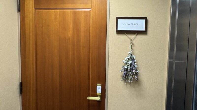 Wooden studio PLAYA door with a sign and a white doorbell above the handle